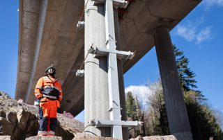 En arbeider i verneutstyr står under en veibro å ser opp.