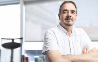 Portrett av Brede Edvardsen, leder i Norsk Arbeidsmandsforbund, som står med armene i kors i et lyst kontorlokale. Han ser fornøyd ut. Bakgrunnen viser et vindu med gardiner og en kontorstol.