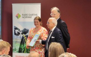 Næringsminister Cecilie Myrseth (Ap) står sammen med hovedeier Stein Sturla Steinsvik og deleier Carl Diderik Cappelen foran en plakat med teksten "Rare Earths Norway." Myrseth holder et dokument mens de smiler til publikum. Foto tatt under en presentasjon.