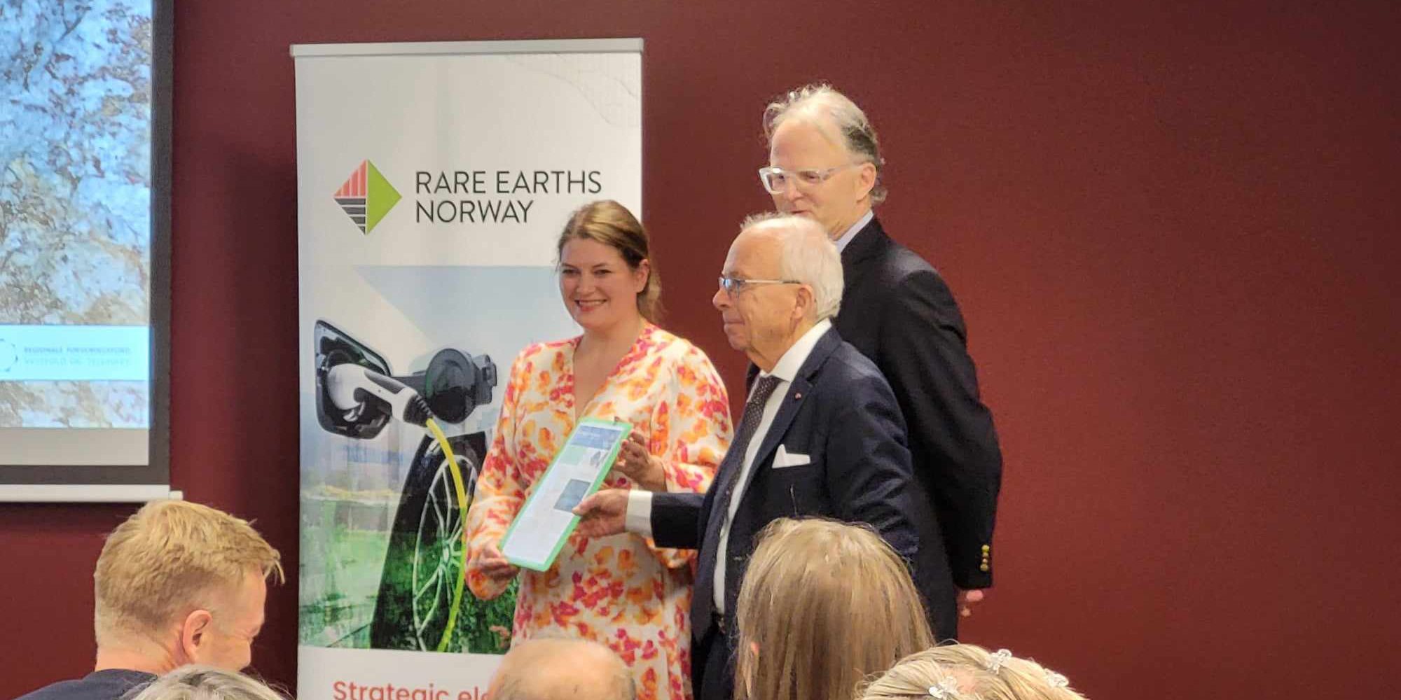 Næringsminister Cecilie Myrseth (Ap) står sammen med hovedeier Stein Sturla Steinsvik og deleier Carl Diderik Cappelen foran en plakat med teksten "Rare Earths Norway." Myrseth holder et dokument mens de smiler til publikum. Foto tatt under en presentasjon.