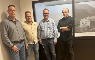 Rune Mjelde, Frank Toks, Svein Jonny Albrigtsen og Arne Presterud står ved siden av hverandre inntil en vegg og smiler.
