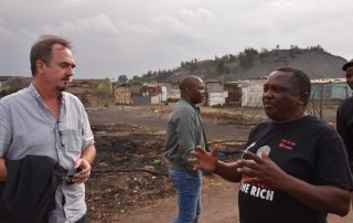 Forbundsleder Brede Edvardsen i samtale med Matthews Hlabane fra South African Green Revolutionary Council, med en bakgrunn av enkle bygninger og landskap fra slummen.