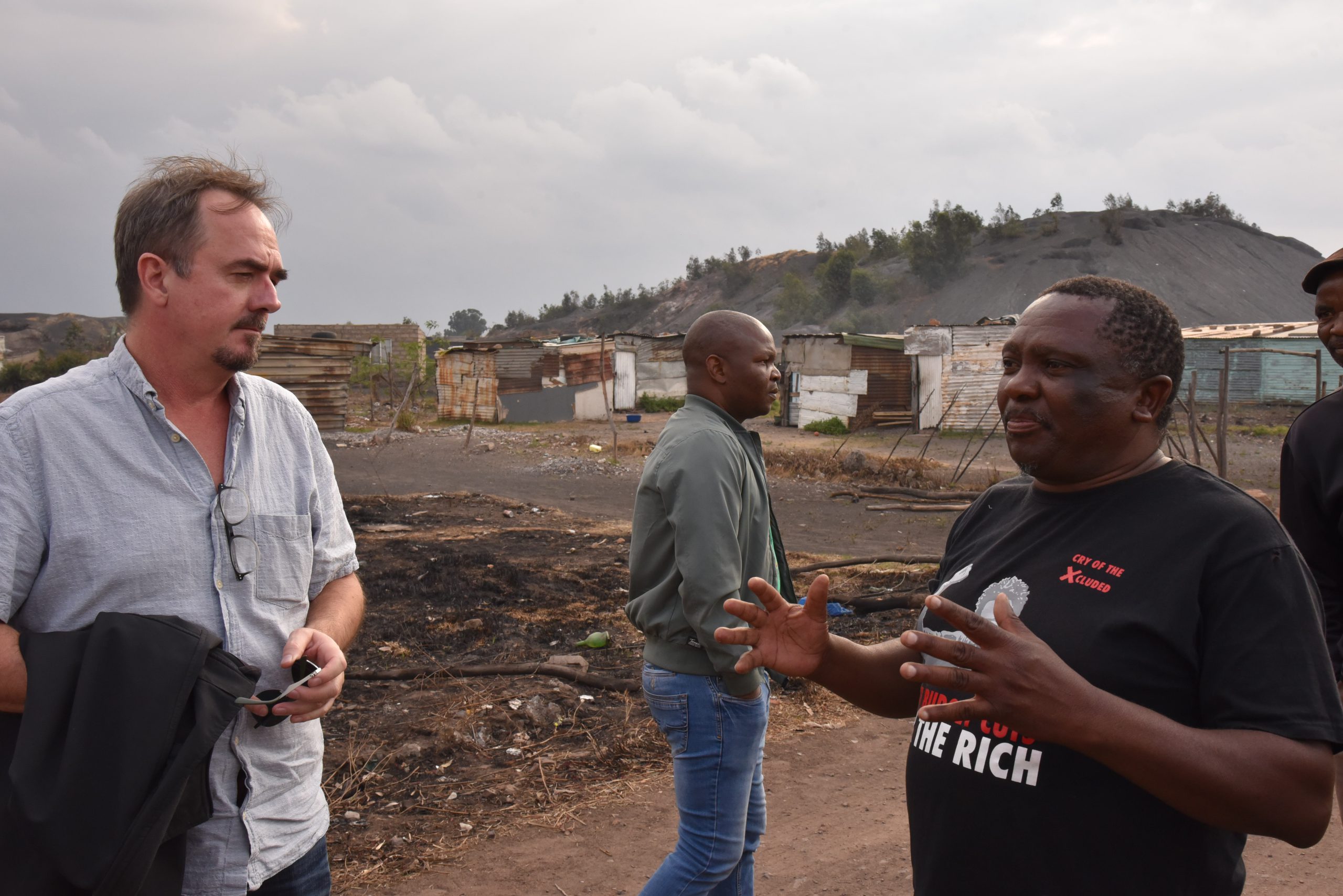 Forbundsleder Brede Edvardsen i samtale med Matthews Hlabane fra South African Green Revolutionary Council, med en bakgrunn av enkle bygninger og landskap fra slummen.